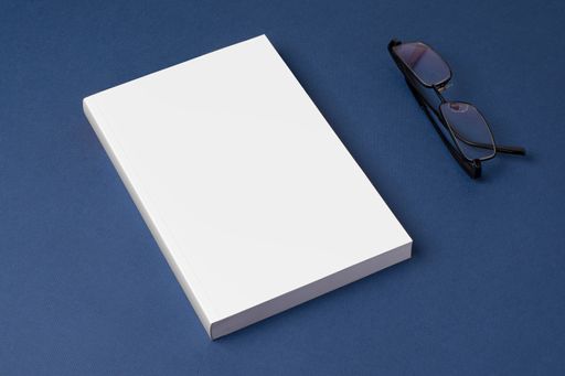 A closed novel book with blank cover on a blue surface with glasses - editable mockup template