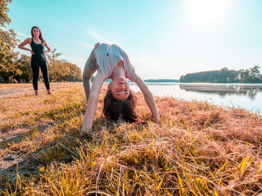A young girl doing the bridge pose on dry grass next to a lake
