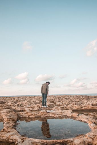 A man strolling on a rocky shore by the ocean under a cloudy blue sky