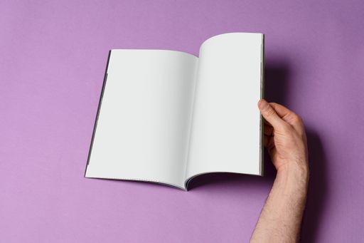 A male hand opening a book catalog with blank pages on purple surface - editable mockup template