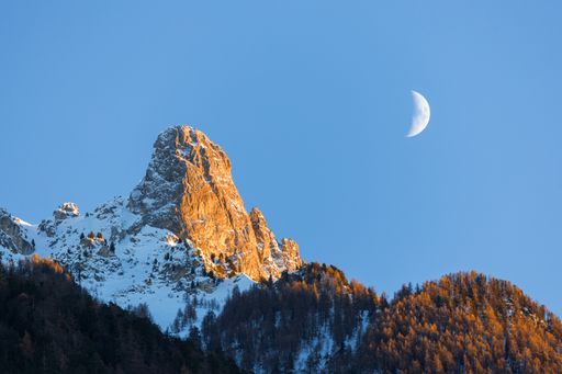 Winter landscape view of the moon above the Pierre Avoi mountain illuminated by the setting sun, shot from Saxon Wallis
