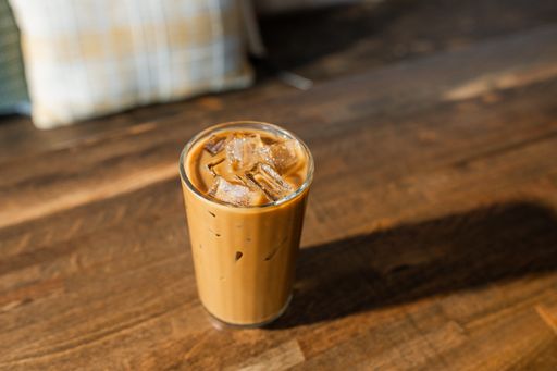 A small glass of iced coffee with ice on a table.