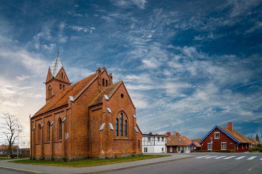 A large terracotta building of a church under blue cloudy sky next to red and white houses