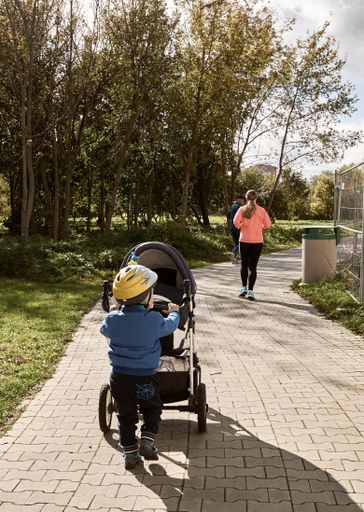 A young boy with safety helmet pushing a baby buggy in the Rataje park