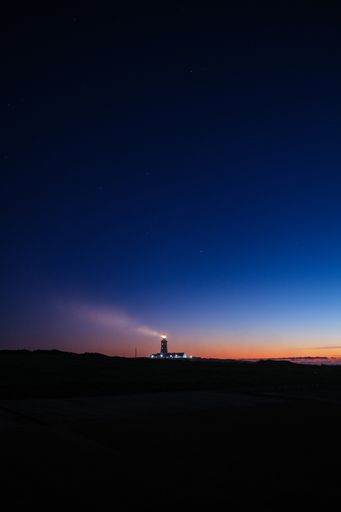 A vertical shot of the night over the silhouette of the land and a lighthouse in the background