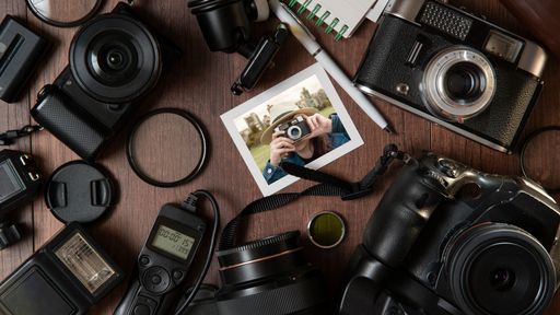 Top view of Photograph of young woman taking a photo, surrounded by flash, filters, lenses, modern and old cameras on a wooden table