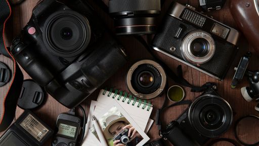Top view of Photograph of young woman taking a photo, surrounded by flash, filters, lenses, modern and old cameras on a wooden table