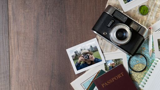 Top view of Photographs of woman taking photos, passports, old photo camera, map and notebook on a dark wooden table