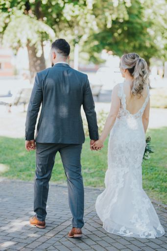 A back view of a stylish wedding couple walking in the park holding hands