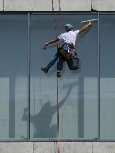 Novi Sad, Serbia - June 30th 2021 - Worker with  helmet on the head cleaning the building's windows hanging on the rope