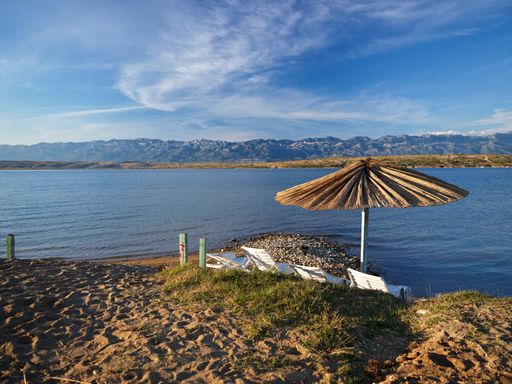 An umbrella and folding chairs on a beach surrounded by the sea on a sunny day in Vrsi, Croatia