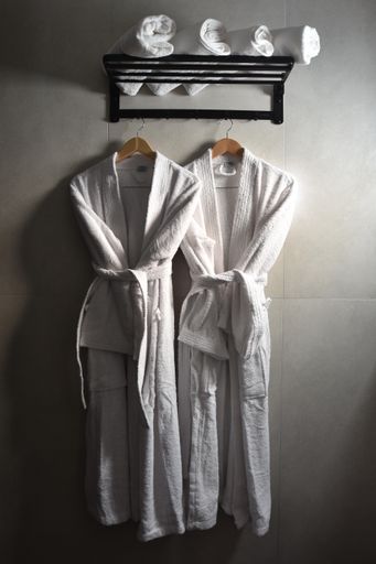 A vertical shot of two spa robes hanging on a black wall rack with rolled up towels on it