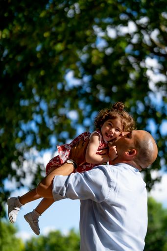 A vertical shot of the father hugging and kissing his daughter in a park
