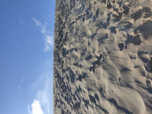 A vertical shot of gray sand dunes under a blue sky