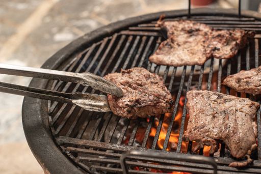 A closeup shot of steak grilling over charcoal outdoors