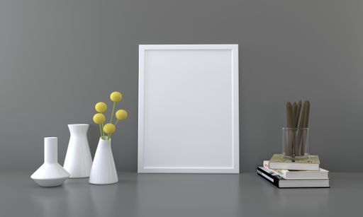 A blank picture frame with vases and books on a table