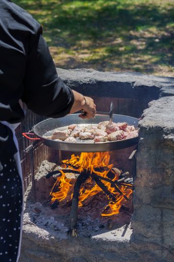 woman frying chicken in a paella pan on the fire in the countryside to make a typical spanish paella