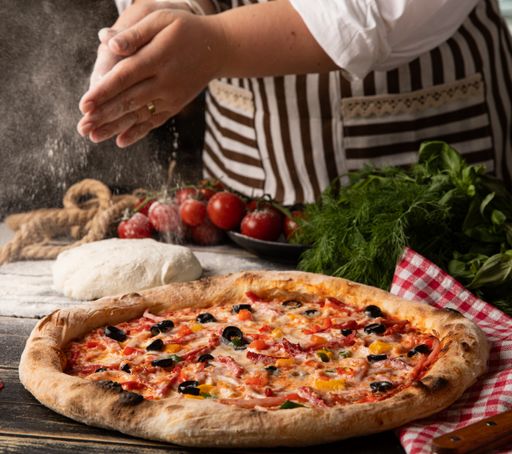 A person adds seasoning to a just-baked pizza
