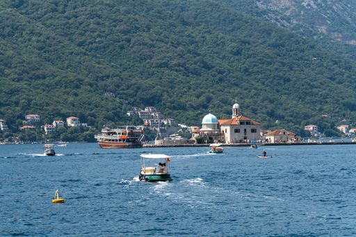 A lone boat floats in the middle of Kotor Bay, going to Our Lady of the Rocks island, Perast, Montenegro