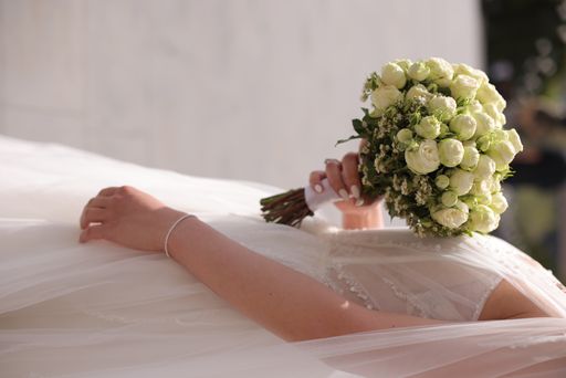 A bride in a veil holding flowers in sunlight.