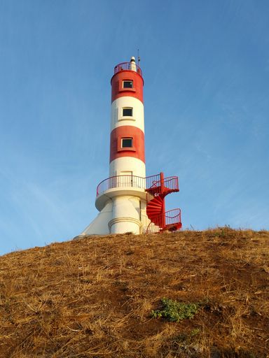 A low angle shot of a red and white lighthouse in the middle of a field on a bright clear summer day