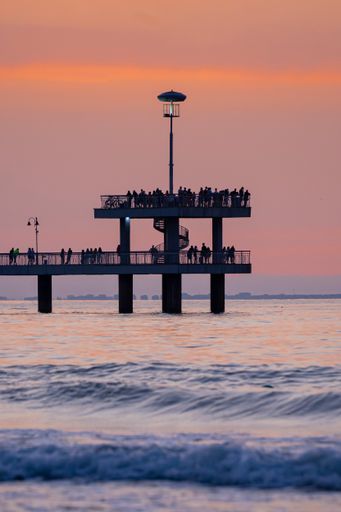 A vertical shot of people on a pier enjoying the view of the calm sea during a scenic sunset