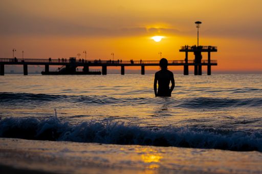 A closeup of a man going into the sea with beautiful orange sunset in the background