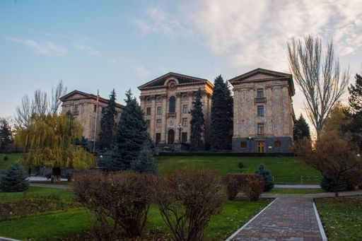 A grand historical building of the Armenian Parliament with a well-maintained garden in front, captured under a partly cloudy sky.