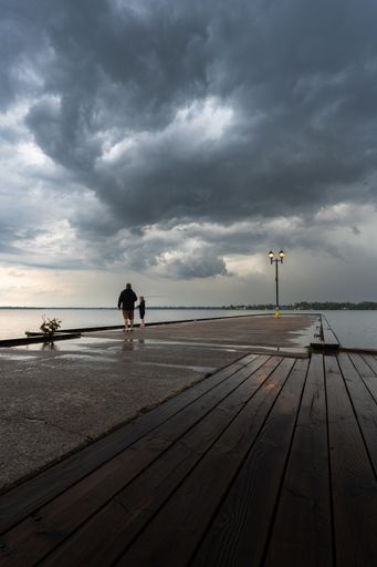 A Father and son fishing off a pier during stormy weather with dramatic clouds over the lake