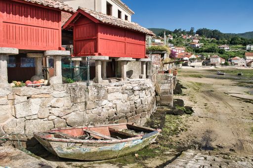 An old abandoned rowing boat next to traditional red granaries at low tide in the town of Combarro, Galicia, Spain.