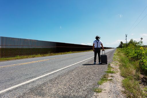 A  person with a gray suitcase next to the wall in Brownsville, Texas