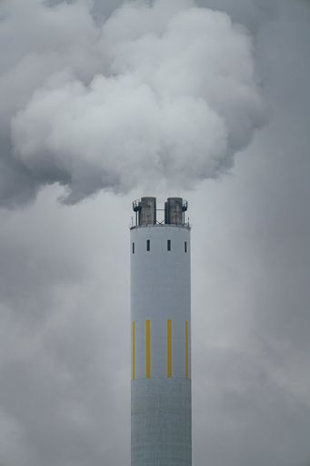 The thick smoke billows from a factory chimney enveloped in clouds on a misty day