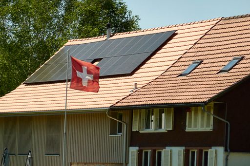 The solar panels on a house roof with a Swiss flag in the foreground