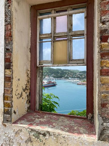 A vertical shot of a window of an abandoned building looking at the sea with ships on it