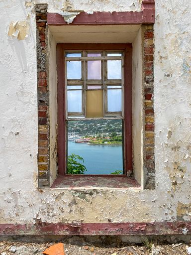 A vertical shot of a window of an abandoned building looking at the sea with ships on it