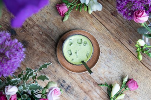 A top view of a glass of matcha on a wooden table among flowers