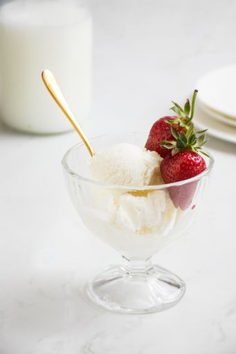 A close-up vertical of vanilla ice cream served in a glass bowl with fresh strawberries and a golden spoon