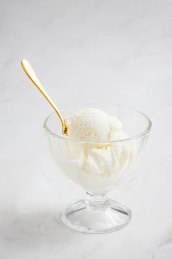 A close-up vertical of a glass bowl with vanilla ice cream and a golden spoon on a white background