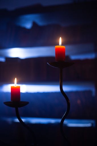 Two lit candles in darkness with glowing blue lights in the background