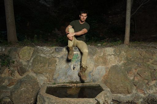 A beautiful shot of young athletic male sitting above an old stone source of drinking water
