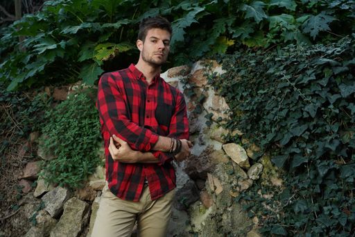 A horizontal shot of an attractive male with a checkered shirt posing against a ruined wall