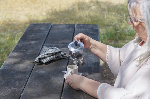 woman seen in profile serving herself a coffee on a wooden table in the countryside