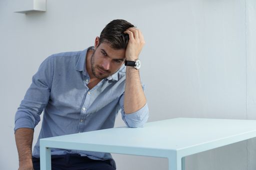 A portrait of a stunning male sitting in a white furnished room with a mild-blue classic shirt