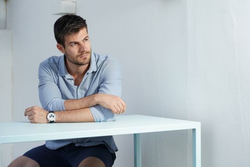 A young Hispanic male wearing a blue shirt posing next to a white desk