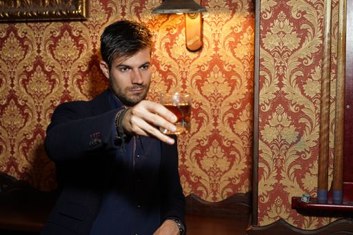 A young Hispanic male in a formal outfit at a restaurant and drinking whiskey