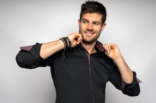 A cheerful young Hispanic male wearing a black shirt standing against a white wall