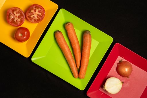 A top view of sliced tomatoes, onions, and carrots on colorful plates on a black table