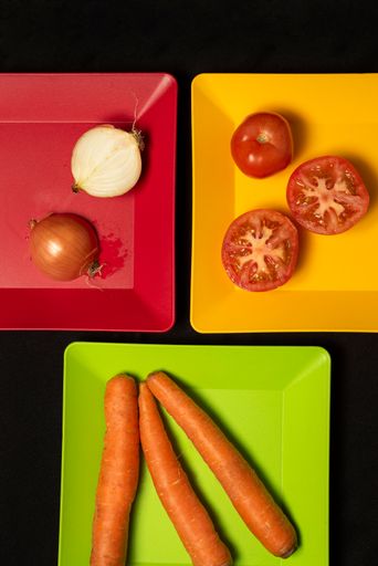 A top view of sliced tomatoes, onions, and carrots on colorful plates on a black table