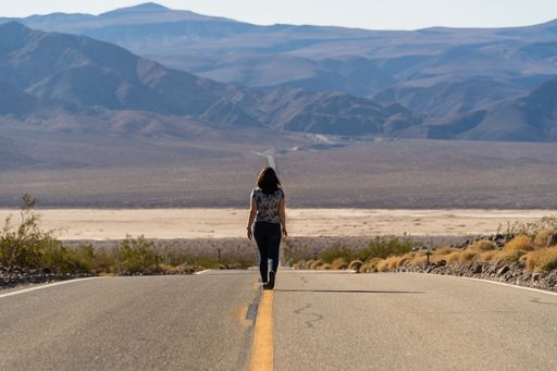 A female walking on the asphalt road looking at mountains in the USA - death valley