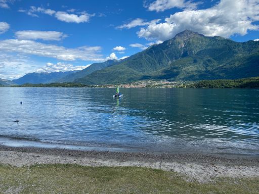 A landscape of a lake surrounded by hills covered in greenery under the sunlight and a blue cloudy sky